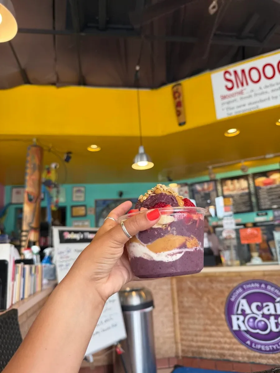 A loaded açaí bowl held up at the Paradise Yogurt counter, with the teal walls and yellow ceiling behind it