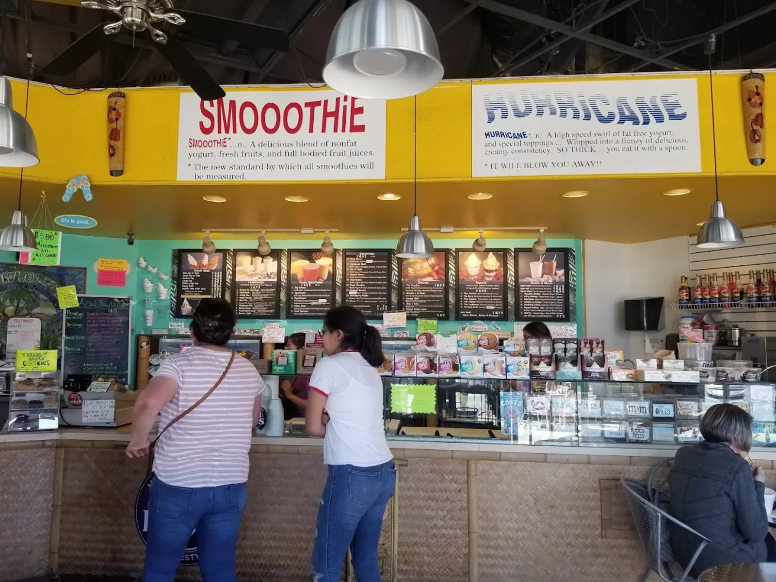 Inside Paradise Yogurt: the counter with the hand-painted Smoothie and Hurricane signs, pendant lights and customers ordering